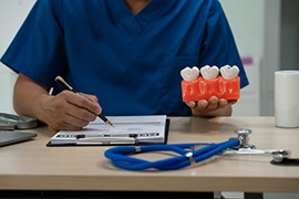 Dentist holding a huge model of three teeth while completing paperwork