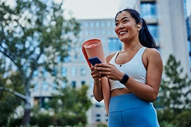 Smiling woman walking on park with workout mat